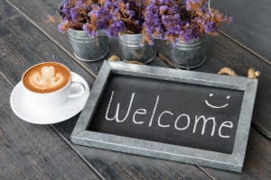 chalkboard with welcome message on table with coffee and flowers